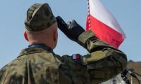 Żołnierz salutujący przed flagą Polski